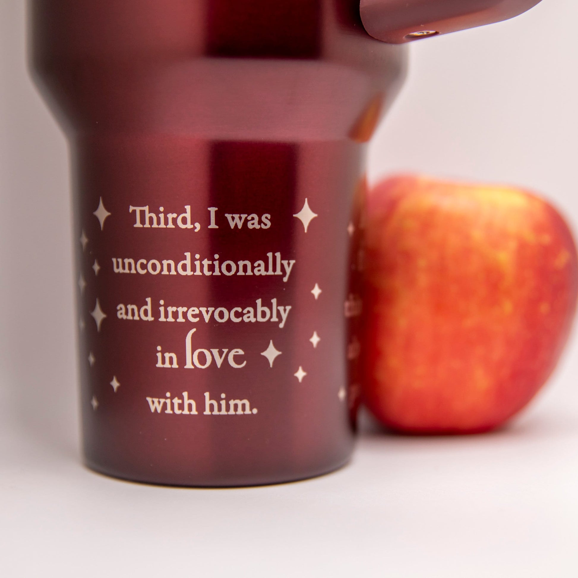 a red travel mug with a quote on it next to an apple