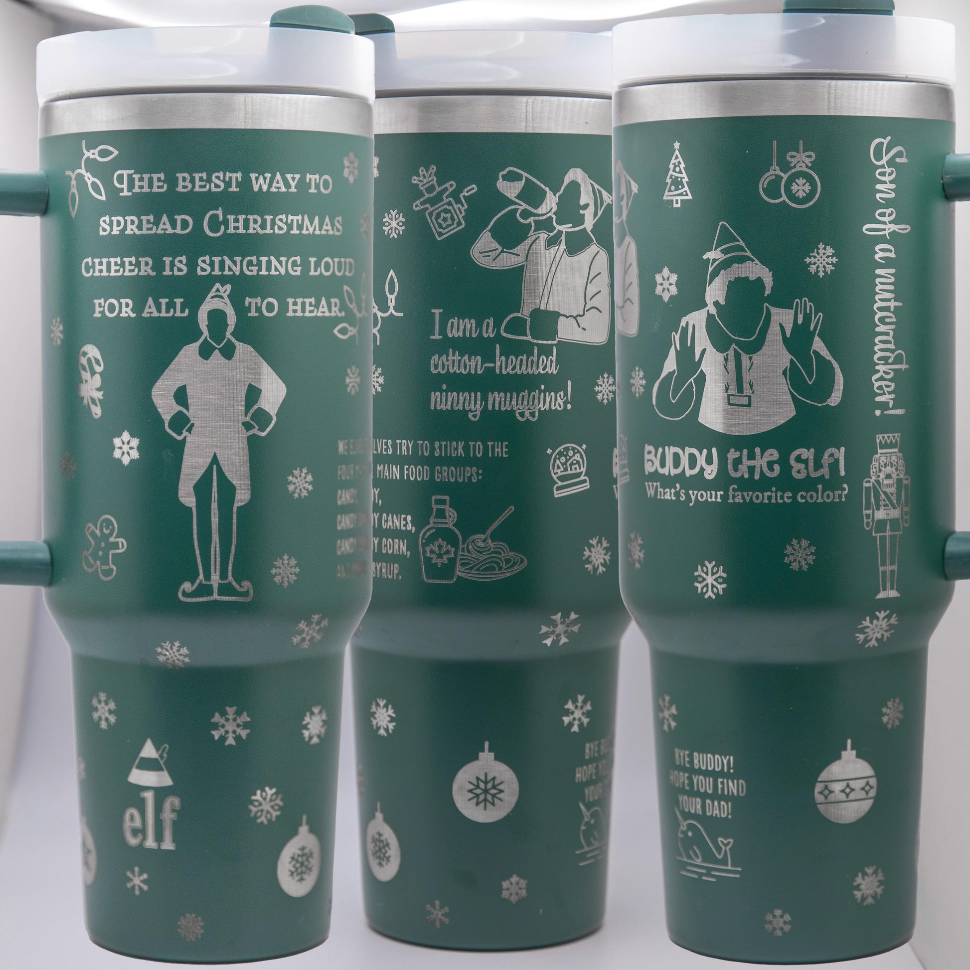 two travel mugs sitting next to a christmas tree